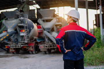 Asian chief engineer standing in cement mixing plant. Background is industrial factory with big cement mixer truck. Material production process and quality control.