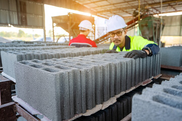 A construction workers wearing protective clothing carefully inspect stacking hollow concrete blocks (concrete blocks) in an indoor factory or construction material storage area.