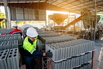 A construction workers wearing protective clothing carefully inspect stacking hollow concrete blocks (concrete blocks) in an indoor factory or construction material storage area.