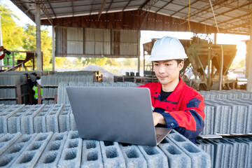 Asian male engineer wearing protective clothing inspecting concrete blocks (cinder blocks) outdoors, wide angle shot.