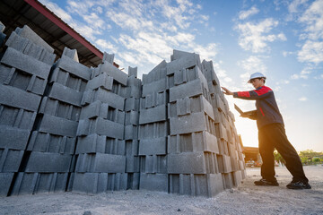 Asian male engineer wearing protective clothing inspecting concrete blocks (cinder blocks) outdoors, wide angle shot.