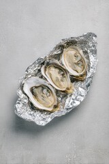 Three open oysters on crinkled foil, flat lay, against light gray backdrop