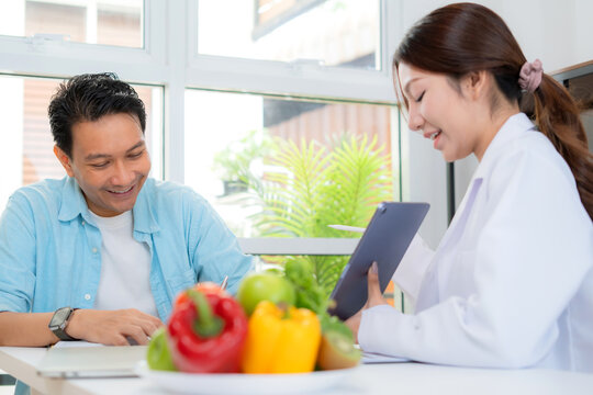 Asian nutritionist using tablet to explaining personalized meal plan with AI to patient during healthcare consultation, healthy lifestyle, woman dietitian showing nutrition plan with AI on tablet.