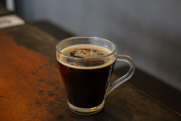 Glass mug of hot black coffee infused with fresh ginger slices on a wooden table. Traditional herbal spicy coffee.