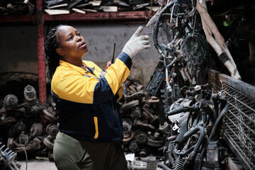 Professional Black female supervisor manager checks auto spare parts stock storage at stack warehouse, communicates job with walkie-talkie in manufacturing factory, and industrial worker occupation.