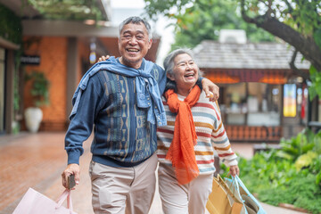Joyful senior asian couple walking with shopping bags at mall smiling and laughing, love retirement lifestyle, shopping happiness and active senior living, purchase sale promotion, retail therapy