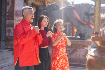 Asian family in red clothes making traditional Chinese New Year greeting gesture at temple,...