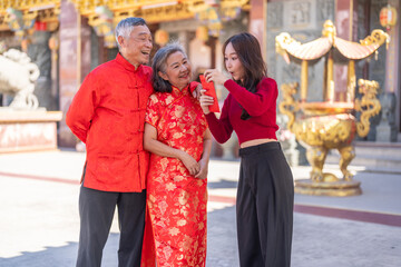 Asian girl happy receiving red envelope from grandparents in traditional chinese clothes, celebrating lunar new year at ornate temple, joyful family moment, culture and love shared between generations