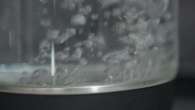 Water Boiling Closeup, Detailed View Of Steaming Kettle Water, Closeup Of Boiling Water Inside Reflective Kettle, Microbubbles Ascend In Glass Kettle Under Subdued Studio Lighting Conditions