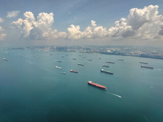 View of numerous cargo ships in the waters near a coastal city with scattered clouds