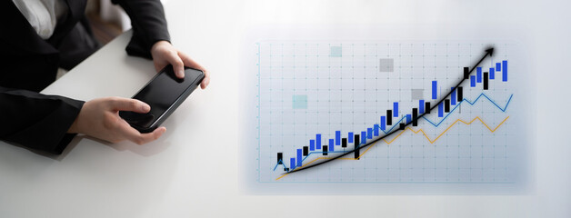 A business professional engages with a smartphone while focused on financial data, showcasing an upward trend on a graph in a modern office setting. Impute
