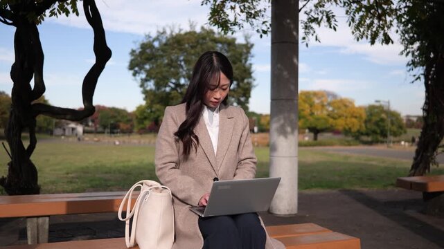 公園のベンチに座りノートパソコンで作業するビジネスウーマン