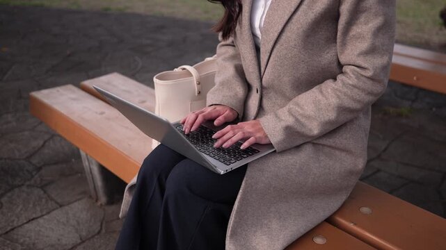 公園のベンチに座りノートパソコンで作業するビジネスウーマンのズームアウト