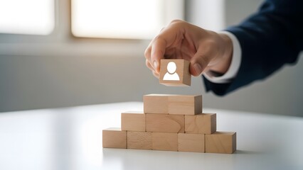 Hand adding wooden block with person icon to a pyramid of blocks team building