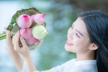 Fotobehang Lotusbloem A young Vietnamese woman in a white ao dai standing by Hoan Kiem Lake, holding a bouquet of pink lotus flowers  © CravenA
