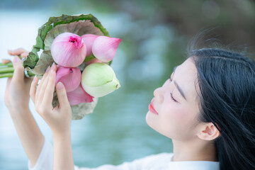 A young Vietnamese woman in a white ao dai standing by Hoan Kiem Lake, holding a bouquet of pink lotus flowers