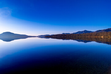快晴の青空の鏡の水面に岸辺の風景を反射する湖。