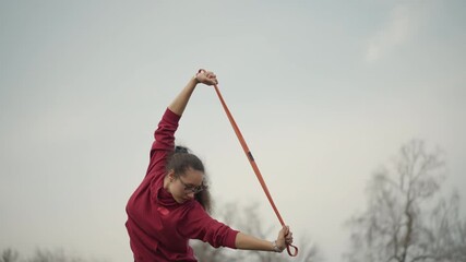 Silhouette Of Woman Flying Ribbon In Sky, Focused Lady Holding Ribbon Against Soft Cloudy Background Outdoors, An Outdoor Scene Capturing Woman Practicing With Ribbon Against Light Cloudy Sky