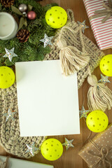 Festive flat lay with blank paper, Christmas gifts, yarn tassels, stars, greenery, and bright pickleballs. Perfect for holiday cards, winter designs, and seasonal invitations.