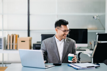 A professional businessman working on a laptop while holding a coffee cup in a modern office, representing productivity