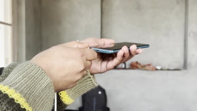Closeup hands of unrecognizable man plugging charging cable into phone and unplugging it, repeating action multiple times standing on room background. Concept of contemporary technology convenience.