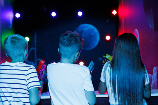 Two boys and a girl playing laser tag in a dark room with bright lights and a planet projection.