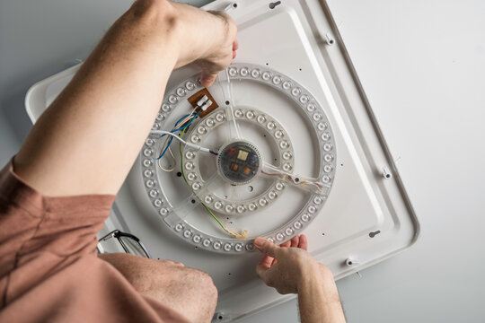 Adult man replaces round LED module on ceiling plate, focused move explains safe electric work and modern reliable home illumination.