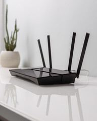 Sleek WIFI router with four antennas on white desk near cactus in pot, minimalist home interior for...
