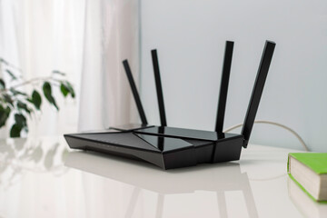 Modern WIFI router with four antennas on white table in bright room with plants and book, home network hub for everyday online life.