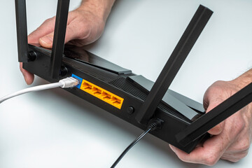 Hands connecting WiFi router with network and power cables on white desk, concept of home internet installation and setup