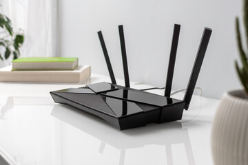 Black WIFI router with four antennas on white desk near books in bright home office interior, symbol of wireless internet connection.