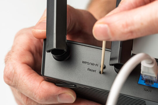 Closeup of hand resetting WiFi router with toothpick through WPS reset hole during internet connection troubleshooting at home