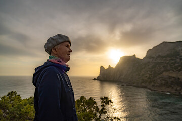 Senior woman sunset mountain looking over the vast sea and dramatic cliff landscape.