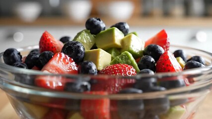 A vibrant and healthy fruit salad with fresh strawberries, blueberries, and avocado in a clear glass bowl, perfect for a nutritious snack or breakfast.