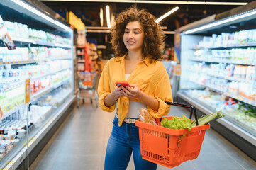 Woman grocery shopping using smartphone in supermarket aisle