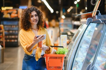 Woman grocery shopping in supermarket checking phone