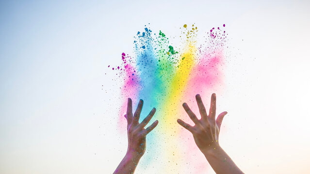 Colorful powder exploding from hands against bright sky  