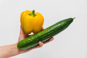 Hand holding a yellow bell pepper and a green cucumber in a simple setting
