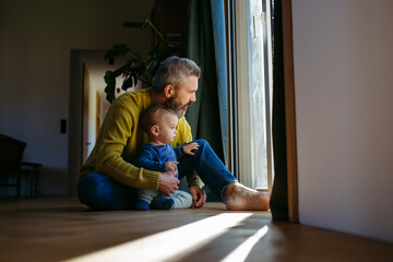 Father with little toddler son looking out of window.