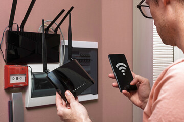 Man configuring WIFI router with smartphone near home network cabinet, checking wireless signal...