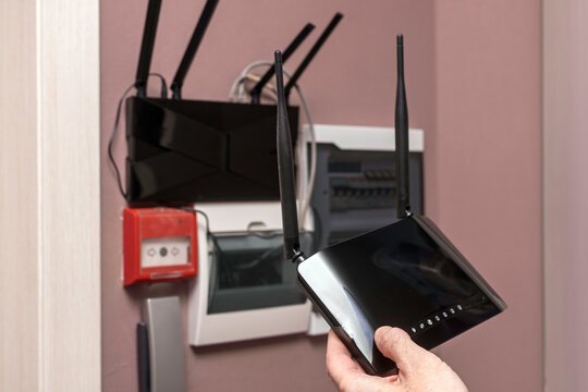 Image shows old 2.4 GHz router in hands, new 5.2 GHz router on wall near home network cabinet, WIFI upgrade for faster connection