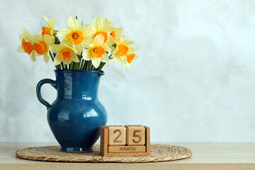Daffodils in vase with march 25 wooden calendar