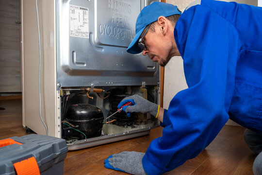 Man repairs refrigerator at home in morning with tools and focused attention