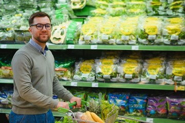 Handsome man with shopping trolley in fruit and vegetable department of supermarket