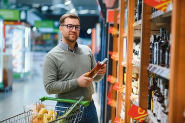 A man takes alcoholic drinks from the supermarket shelf. Shopping for alcohol in the store