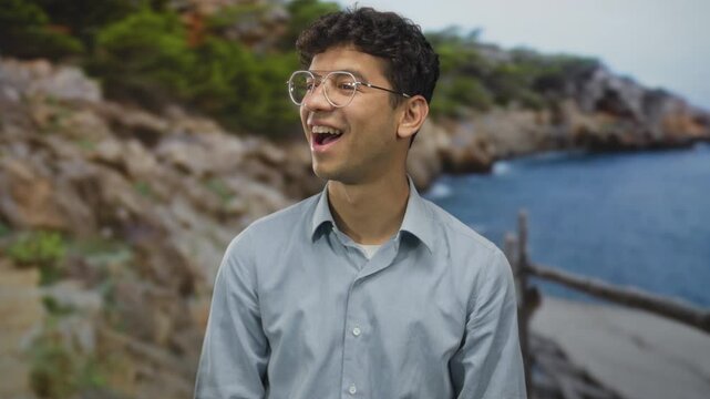 Man with glasses smiling broadly at sunlit beach shoreline under clear blue sky; carefree happiness.