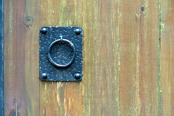 One beautiful ring-shaped knocker on an iron plate on a wooden gate