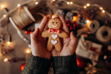 Hand holding a cheerfully decorated gingerbread man cookie, with a colorful, warm Christmas backdrop