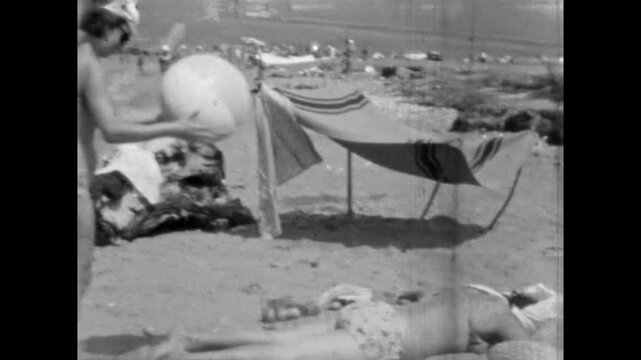 Woman in swimsuit plays with ball on beach, fooling around. Fun, funny vacation with friends by sea. Young female spend time on coast during summer. Old film. Archival retro 1960s. Vintage archive.