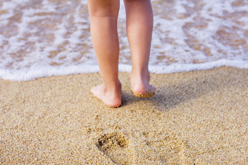 Child's feet standing on the sand at the edge of the sea